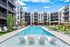 Luxurious apartment complex with a stunning outdoor pool, modern lounge chairs, and stylish architecture under a bright blue sky.