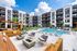 Modern apartment complex with luxurious outdoor pool area, stylish seating, and vibrant landscaping under a bright blue sky.