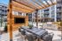 Modern apartment courtyard featuring a stylish outdoor dining area under a wooden pergola, surrounded by lush landscaping, with a swimming pool and contemporary building facade.
