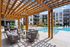 Luxurious apartment complex showcasing a stylish poolside lounge area with modern seating under a wooden pergola, perfect for relaxation and social gatherings.