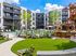Modern apartment complex featuring a luxurious outdoor pool, stylish lounge chairs, and lush greenery under a bright blue sky.