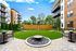 Contemporary apartment complex featuring a lush green courtyard with cozy seating and fire pit, bordered by stylish multi-story buildings.