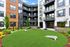 Modern apartment complex with lush green courtyard featuring a lawn area for relaxing and games, surrounded by stylish multi-story building with balconies.