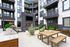 Modern apartment courtyard featuring stylish outdoor seating, a brick fireplace, and lush greenery, surrounded by elegant balconies.