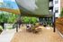Inviting outdoor space with shaded seating area, modern apartment backdrop, and lush greenery, perfect for relaxation and gatherings.