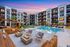 Modern apartment complex with a luxurious poolside area, featuring cozy fire pits and stylish outdoor seating under a vibrant sunset sky.