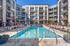 Luxurious apartment complex featuring a sparkling outdoor pool, surrounded by sun loungers and modern multi-story buildings with balconies.