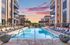 Luxurious apartment complex featuring a sparkling pool, modern sun loungers, and stylish architecture against a vibrant sunset sky.
