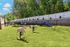 Inviting outdoor playground area with lush green grass, playful horse jumping obstacle, and colorful climbing ramp amidst scenic woodland backdrop.
