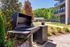 Inviting outdoor barbecue area with a modern grill, surrounded by lush greenery, perfect for gatherings at a stylish apartment complex.