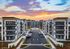 Modern apartment complex with stylish architecture, lush landscaping, and welcoming entrance, set against a stunning sunset backdrop.
