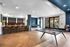 Modern communal area featuring a stylish bar with sleek stools, a ping pong table, and bright natural lighting from large windows.