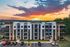 Modern apartment building with contemporary design, featuring large balconies and ample parking, set against a stunning sunset backdrop.