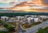 Aerial view of modern apartment complex surrounded by lush greenery with a stunning sunrise backdrop, showcasing contemporary architecture and serene living.