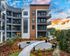 Modern four-story apartment building with spacious balconies, surrounded by lush gardens and a vibrant sunset backdrop.