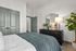 Elegant bedroom with modern decor, featuring a cozy bed, stylish dresser with a unique table lamp, and lush green plant.