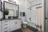 Modern bathroom featuring sleek white cabinetry, elegant black fixtures, stylish decor accents, and a refreshing shower-tub combination.