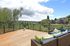 Spacious balcony with cozy seating, offering stunning panoramic views of lush greenery and a vibrant neighborhood under a bright blue sky.