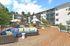 Modern apartment complex with a spacious wooden deck, cozy outdoor seating, and vibrant greenery under a clear blue sky.