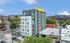 Modern multi-story apartment building with a rooftop terrace, surrounded by vibrant city views and lush greenery.