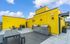 Vibrant rooftop terrace with striking yellow walls, modern outdoor seating, and built-in stainless steel grills under a clear blue sky, offering an inviting space for outdoor dining and entertainment.