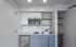 Modern small kitchen with sleek blue cabinets, built-in microwave, and stylish open shelving, ideal for compact living spaces.