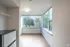 Bright corner room with large windows overlooking lush greenery, featuring sleek flooring and a modern stainless steel fridge.