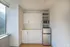 Bright modern kitchenette with sleek cabinetry, built-in microwave, and compact refrigerator, illuminated by natural light from a large window.