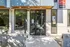 Contemporary apartment entrance with elegant glass doors, surrounded by lush greenery and modern design elements.