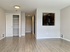 Modern apartment interior with elegant wooden flooring, spacious layout, and a kitchen with sleek dark cabinets.