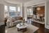 Bright and inviting living room with large bay windows and elegant dining area featuring a charming brick accent wall.