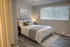 Inviting bedroom with modern decor, featuring a plush queen-sized bed, soft lighting, and large window with blinds.