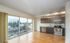 Modern apartment with floor-to-ceiling windows offering a scenic view, featuring a sleek kitchen with stainless steel appliances and hardwood flooring.