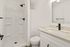 Modern bathroom featuring a sleek walk-in shower with black fixtures, elegant white vanity with black faucet, and minimalist design.