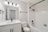 Modern bathroom with elegant white vanity, sleek black fixtures, and a pristine tiled bathtub.