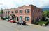Charming red brick building with green window frames, surrounded by lush greenery and parked cars, offering a welcoming residential feel.