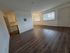 Inviting living space with elegant wood flooring, large windows providing natural light, and a glimpse of a modern kitchen with white cabinetry.