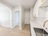 Elegant kitchen with sleek countertops, modern white cabinets, and stylish gold hardware, leading into a bright hallway with wooden floors.