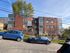 Charming brick apartment building with large windows, surrounded by lush greenery and parked cars, under a clear blue sky.