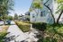 Charming residential street featuring a modern house with well-maintained hedges, lush trees, and a sunny sidewalk.