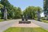 Iconic large W sculpture on a brick platform flanked by towering stone columns and lush green trees in a scenic roadway setting.