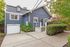 Charming navy blue house with a spacious driveway, inviting front porch, and lush greenery, exuding a cozy and welcoming atmosphere.