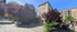 Charming apartment building nestled among lush trees on a sunny, cobblestone street, offering a serene urban living experience.