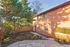 Charming brick apartment with vibrant red door, surrounded by lush greenery and a cozy patio space.