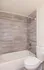 Modern bathroom highlighting sleek grey tile walls, a pristine white bathtub, and contemporary fixtures.