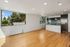 Bright, open-concept living area with sleek wooden floors, modern kitchen with blue tile backsplash, and large windows offering a serene view of lush greenery.