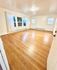 Bright, spacious room with polished hardwood floors, large windows, and elegant white curtains.