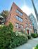 Charming red brick apartment building featuring classic architecture, lush green landscaping, and sunny windows, offering urban living with a cozy atmosphere.