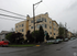 Charming multi-level apartment building with beige siding, nestled on a quiet urban street with lush green landscaping.