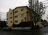 Charming yellow apartment building with multiple floors, surrounded by lush greenery and a white picket fence, perfect for comfortable urban living.